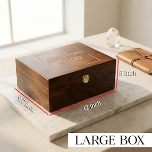 May include: A rectangular dark brown wooden box with a hinged lid and a gold-coloured metal latch. The lid features the engraved text CUSTOM LOGO. Dimensions are 12 inches in length, 9.7 inches in width, and 5 inches in height.