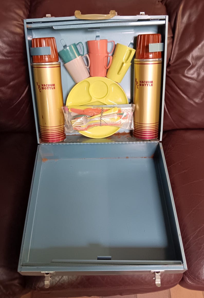 May include: Vintage picnic set in a blue metal case. Includes two gold vacuum bottles with red accents, colorful cups, plates, and cutlery. The vacuum bottles have the text "VACUUM BOTTLE".
