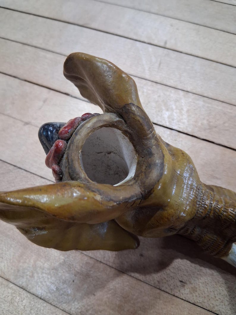 May include: A detailed, close-up view of a ceramic dog head, likely a decorative item. The dog's head is painted in shades of brown and tan, with visible details of the snout, mouth, and ears. The interior of the mouth is red and black.