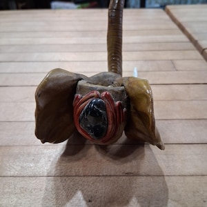 May include: A handcrafted, brown elephant sculpture with large, textured ears and a long, curved trunk. The elephant's face features a dark, glossy stone and red accents, creating a unique and artistic piece.