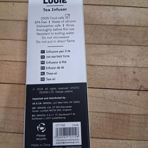 May include: A white and black box for a tea infuser, with the name "LOUIE" at the top. The box includes text about the product's features, such as being food safe and dishwasher safe. The box also has a recycling symbol.