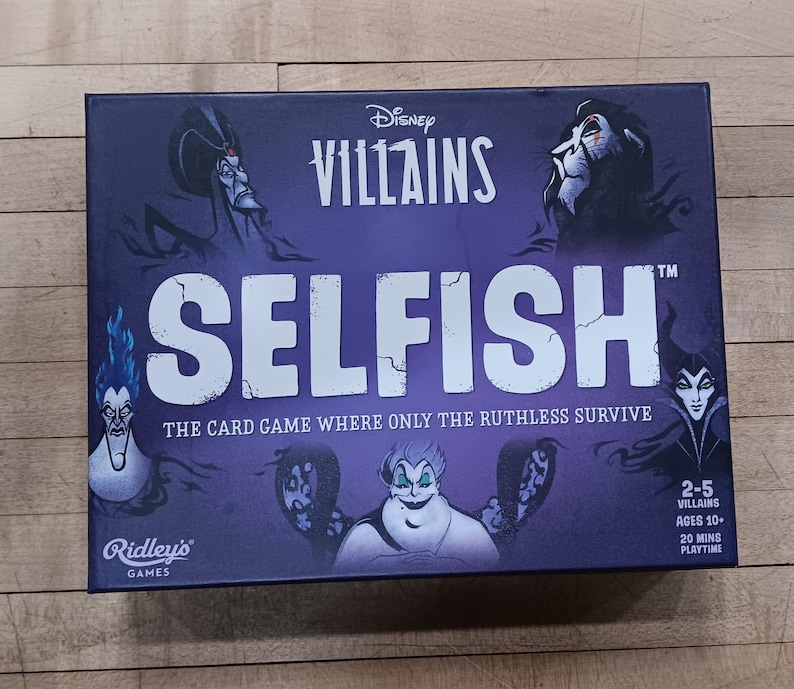 Puede incluir: Una caja de juego de mesa de color p&uacute;rpura con el t&iacute;tulo "Disney Villains Selfish" en texto blanco. La caja presenta im&aacute;genes de villanos de Disney, incluyendo a &Uacute;rsula, Mal&eacute;fica y Scar. El juego es para 2-5 jugadores, de 10 a&ntilde;os en adelante, y dura 20 minutos.