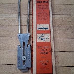 May include: An Apex Keen Edge combination glass cutter, knife, and scissors sharpener. The metal tool has a handle and a blade-like section with a screw. The box is red and orange with text that reads "Cuts faster than a diamond."
