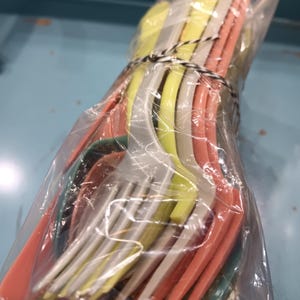 May include: A bundle of colorful plastic forks in a clear plastic bag. The forks are in shades of yellow, white, orange, and teal, tied together with black and white twine. The forks are for a picnic or party.