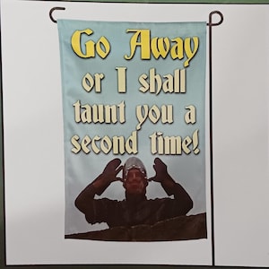 May include: A decorative garden flag with the text "Go Away or I shall taunt you a second time!" in yellow and white. The flag features an image of a person in medieval armor. The flag is attached to a black metal pole.