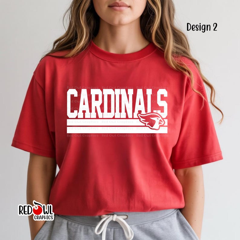 May include: Red t-shirt with the word "CARDINALS" in white block letters and a white bird logo. The shirt also has the text "Design 2" in the upper right corner and the Red Owl Graphics logo in the lower left corner.