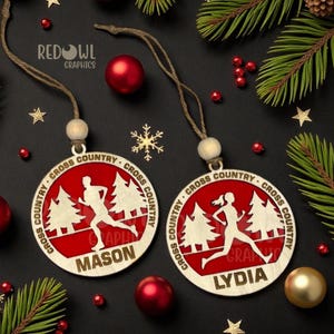 May include: Two wooden Christmas ornaments with a red background and the words "Cross Country" around the edge. One ornament says "Mason" and the other says "Lydia". The ornaments have a running figure and trees.