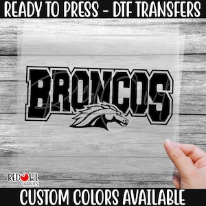 May include: Black and white iron-on transfer design of the word "Broncos" with a stylized horse head.  The design is ready to press onto fabric.