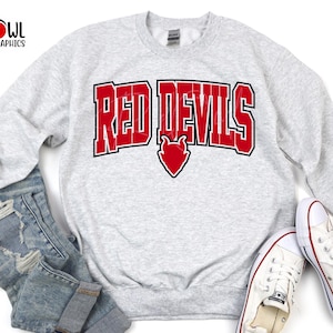 May include: A gray sweatshirt with the text "Red Devils" in red letters with a red devil heart graphic. The sweatshirt is on a blue denim background.