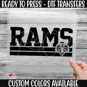May include: Black and white iron-on transfer design featuring the word "RAMS" with a ram's head logo.  The design is ready to press onto fabric.