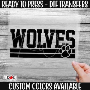 May include: Black and white iron-on transfer design featuring the word "WOLVES" in bold letters with a paw print below. The design is ready to press onto fabric.