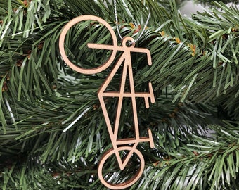 May include: Wooden ornament shaped like a bicycle, hanging from a silver string on a green Christmas tree.