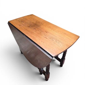May include: A wooden drop-leaf table with a rectangular top featuring a visible wood grain pattern. The table has a dark brown finish and is supported by four turned legs with a spiral design, connected by a lower stretcher base structure.