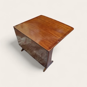 May include: A wooden drop-leaf table with a rectangular top and a rich, warm brown finish. The table has a drop-leaf design, allowing for adjustable size. The table is supported by four legs. The table measures approximately 76 cm long and 76 cm wide.