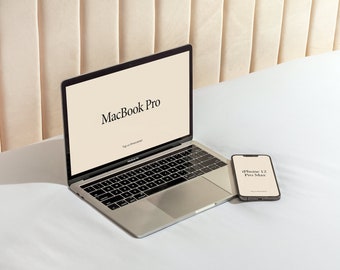 Może przedstawiać: Srebrny laptop MacBook Pro z logo Apple i tekstem "MacBook Pro" wyświetlanym na ekranie. Czarny iPhone 12 Pro Max leży obok laptopa na białej powierzchni.