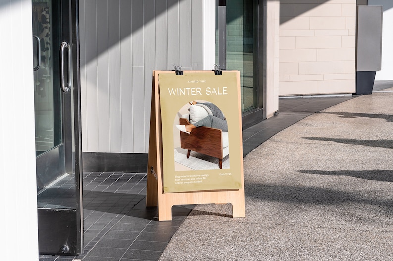 Peut inclure: Un panneau en bois brun en forme de A avec une affiche beige qui dit "Winter Sale" et pr&eacute;sente une photo d'une personne assise dans un fauteuil brun. Le panneau est devant un magasin avec une porte en verre.