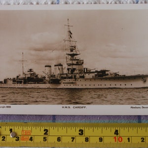 May include: A black and white vintage postcard featuring a photograph of a warship, the H.M.S. Cardiff, at sea. The postcard is titled "H.M.S. CARDIFF." and includes the text "Copyright 2523" and "Abrahams, Devonport."