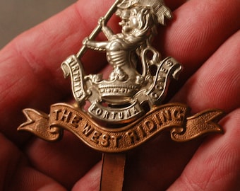 May include: A detailed metal emblem with a lion-like figure holding a flag. The emblem features the words "VIRTUTIS FORTUNA COMES" and "THE WEST RIDING" in a banner design. The emblem is a mix of silver and gold tones.