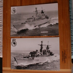 May include: Two monochrome photographs of the HMS Beaver, a warship, at sea. The ship is shown in profile, with its name and number clearly visible. The images are presented on a wooden surface, with a crest in the top left corner.