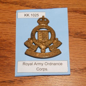 May include: A brass Royal Army Ordnance Corps badge, featuring a crown, shield, and the text "Royal Army Ordnance Corps." The badge is mounted on a blue card with the text "KK.1025."