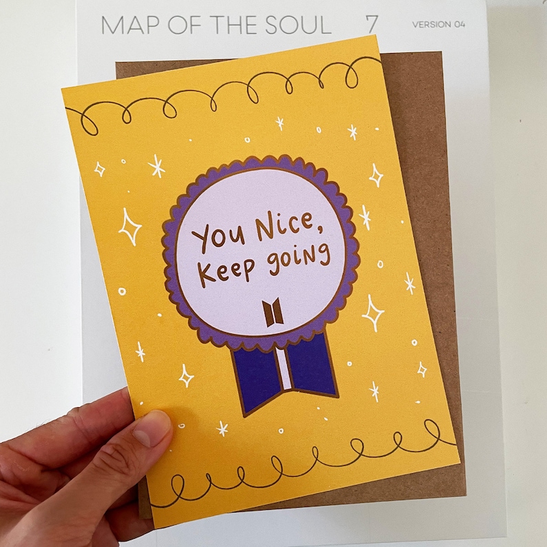 May include: A yellow card with a purple and blue ribbon and a purple circle with the text "You Nice, Keep going" in white. The card has a white background and the text "MAP OF THE SOUL 7" in black.