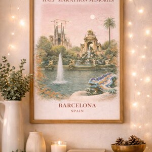 Op de afbeelding: Een ingelijste print met de tekst "HALF MARATHON MEMORIES" en "BARCELONA SPAIN". Het kunstwerk toont een schilderachtig uitzicht op een fontein en gebouwen. De print wordt tentoongesteld op een houten plank met een witte vaas, kaars, boeken en een gouden kom.