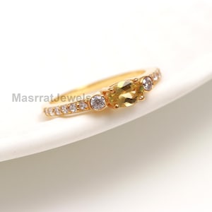 Peut inclure: Une bague en or avec une pierre ovale jaune et de petites pierres claires autour de la bande.