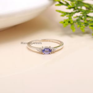 Peut inclure: Une bague en argent avec une pierre ovale violette et deux petites pierres claires de chaque côté. Le texte 'MasrratJewels' est imprimé sur le fond.