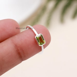 May include: A silver ring with a green gemstone. The gemstone is a rectangular emerald cut.