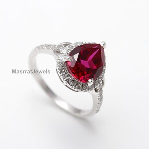 Op de afbeelding: Een ring met een peervormige robijn met een halo van kleinere diamanten, gezet in zilver.
