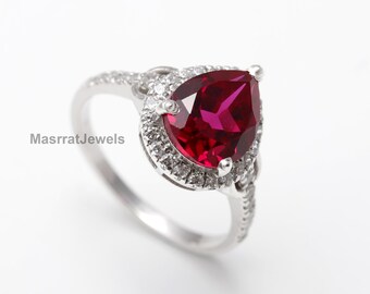 May include: A pear-shaped ruby ring with a halo of smaller diamonds set in silver.