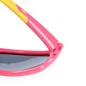 Puede incluir: Gafas de sol rosas y amarillas con un detalle de bisagra. Las gafas tienen lentes grises oscuras.