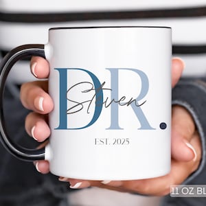 May include: White ceramic mug with a black handle and rim, featuring the text "DR. Steven" in blue and gray, with "EST. 2025" below. The mug is labeled "11 OZ BLACK".