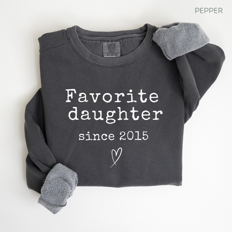Pode incluir: Camisola cinza escuro com o texto branco "Favorite daughter since 2015" e um s&iacute;mbolo de cora&ccedil;&atilde;o. As mangas s&atilde;o dobradas. A camisola &eacute; feita de um material macio.