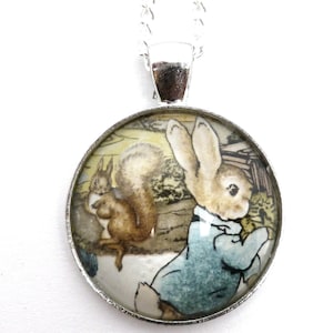 May include: A silver chain necklace with a round glass pendant featuring a vintage illustration of Peter Rabbit in a blue jacket with a squirrel behind him.