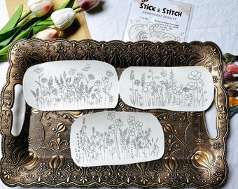May include: Three white embroidery patterns on a gold tray. The patterns are of different floral designs. The tray has a decorative, ornate design. The text on the package reads "Stick & Stitch Embroidery Designs".