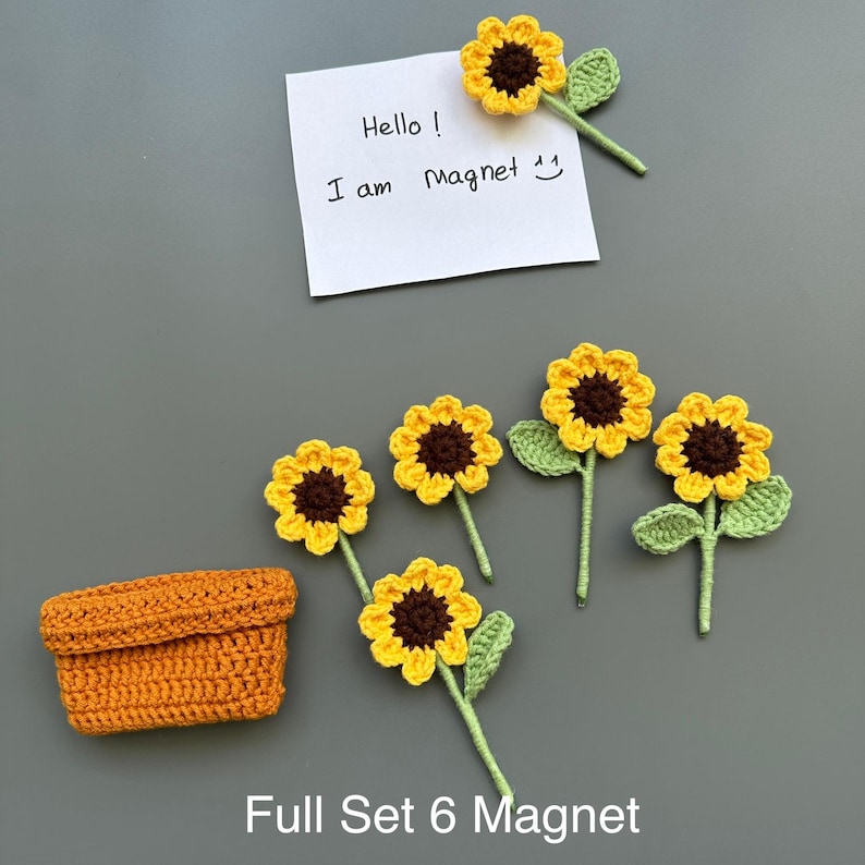 May include: A set of six crochet sunflower magnets with yellow petals and brown centers, along with a small orange crochet basket. A note says "Hello! I am Magnet". The text "Full Set 6 Magnet" is also visible.
