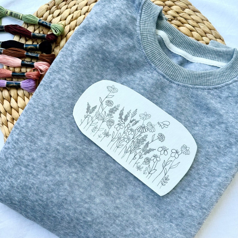 May include: A gray sweatshirt with a white paper pattern of a line drawing of a field of flowers.