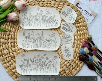 May include: A collection of embroidery designs featuring floral patterns. The set includes seven pre-printed designs, with a ruler showing inches. The designs are accompanied by embroidery floss in various colors. The text "Stick & Stitch Embroidery Designs" is visible.