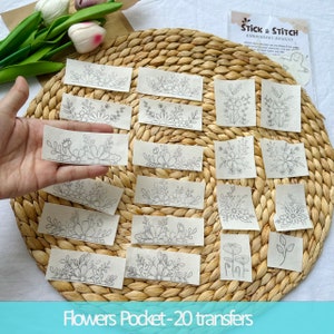 May include: Twenty white fabric squares with black floral embroidery designs. The squares are arranged in a circle on a woven straw surface. The text "Stick & Stitch Embroidery Designs" is visible in the upper right corner of the image. The text "Flowers Pocket - 20 transfers" is visible at the bottom of the image.