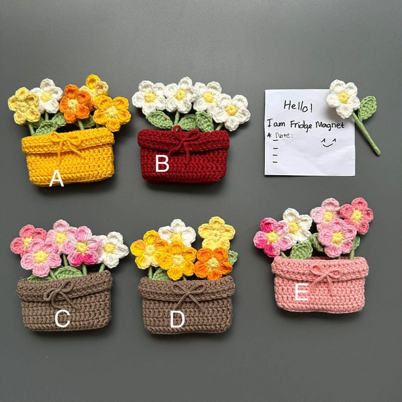 May include: Crocheted flower magnets in various colors, including yellow, red, brown, and pink. Each magnet features a basket of flowers with a bow. A handwritten note says "Hello! I am Fridge Magnet".
