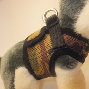 Pu&ograve; includere: Un'imbracatura per cani mimetica nera e marrone con un pannello in rete e un anello in metallo argentato.