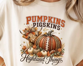 May include: A cream-colored t-shirt featuring a graphic print with the text PUMPKINS PIGSKINS & Highland Things. The design includes a Highland cow with a leopard print bow, a football-textured pumpkin, smaller pumpkins, and autumn leaves.