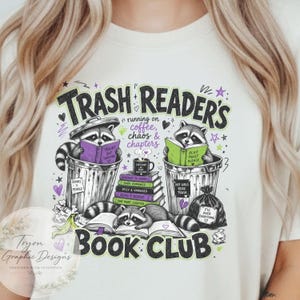 May include: Cream-colored t-shirt with a graphic design featuring raccoons reading books in trash cans and on the ground. The text reads "Trash Reader's Book Club" with additional phrases like "running on coffee, chaos & chapters."