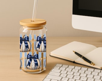 May include: A clear glass tumbler with a bamboo lid and a clear straw, featuring a repeating pattern of beige and white plaid pumpkins adorned with large, dark blue satin bows, set against a background of vertical light blue brush strokes.