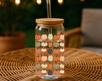 May include: A clear glass tumbler with a bamboo lid and a glass straw, featuring a repeating pattern of small pumpkins in various shades of orange, white, grey, and black. The design covers the exterior of the cylindrical drinking glass.