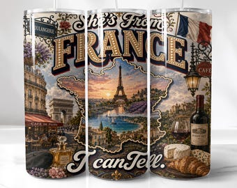 May include: A cylindrical tumbler featuring a collage of French landmarks including the Eiffel Tower, Arc de Triomphe, and a French flag. The text reads She's From FRANCE I can Tell. It includes illustrations of a perfume bottle, wine, cheese, and a croissant.