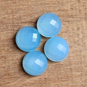 May include: Four light blue chalcedony cabochons with faceted edges. The cabochons are round and have a smooth, polished surface.