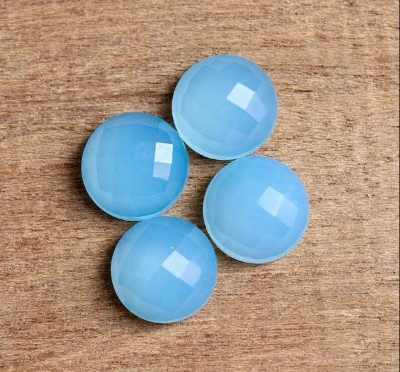 May include: Four light blue chalcedony cabochons with faceted edges. The cabochons are round and have a smooth, polished surface.
