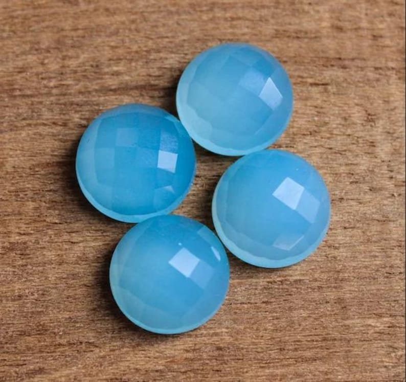 May include: Four light blue gemstone cabochons with faceted surfaces. The cabochons are round and have a smooth, polished finish.